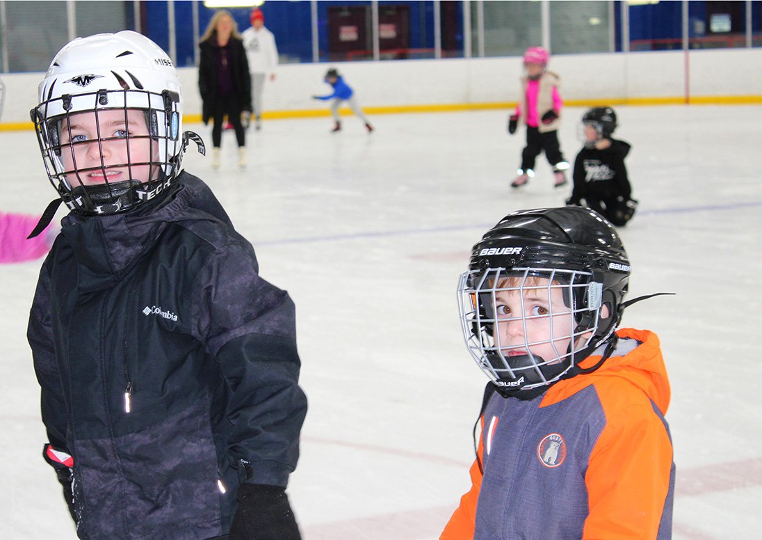 Two boys in hockey helmets skating at Seymour-Hannah Sports and Entertainment Centre.