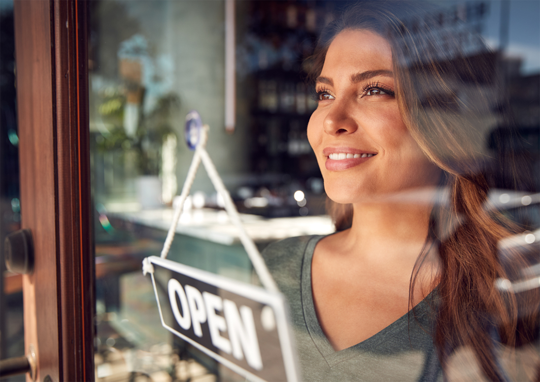 Woman looks out store window above open sign